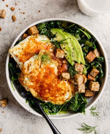 white bowl filled with greens, eggs, avocado and croutons