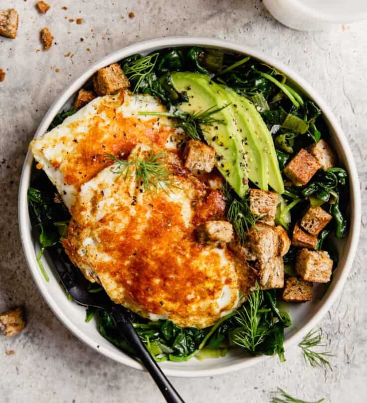 white bowl filled with greens, eggs, avocado and croutons