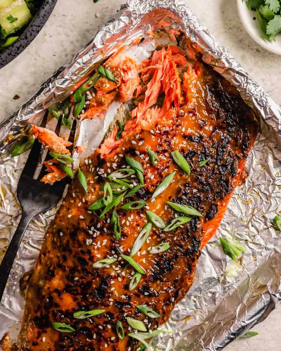 glazed salmon fillet on a foil-lined baking sheet topped with green onions and sesame seeds