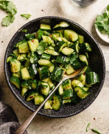 diced cucumbers in a black bowl with a spoon in it—set on a table with cilantro