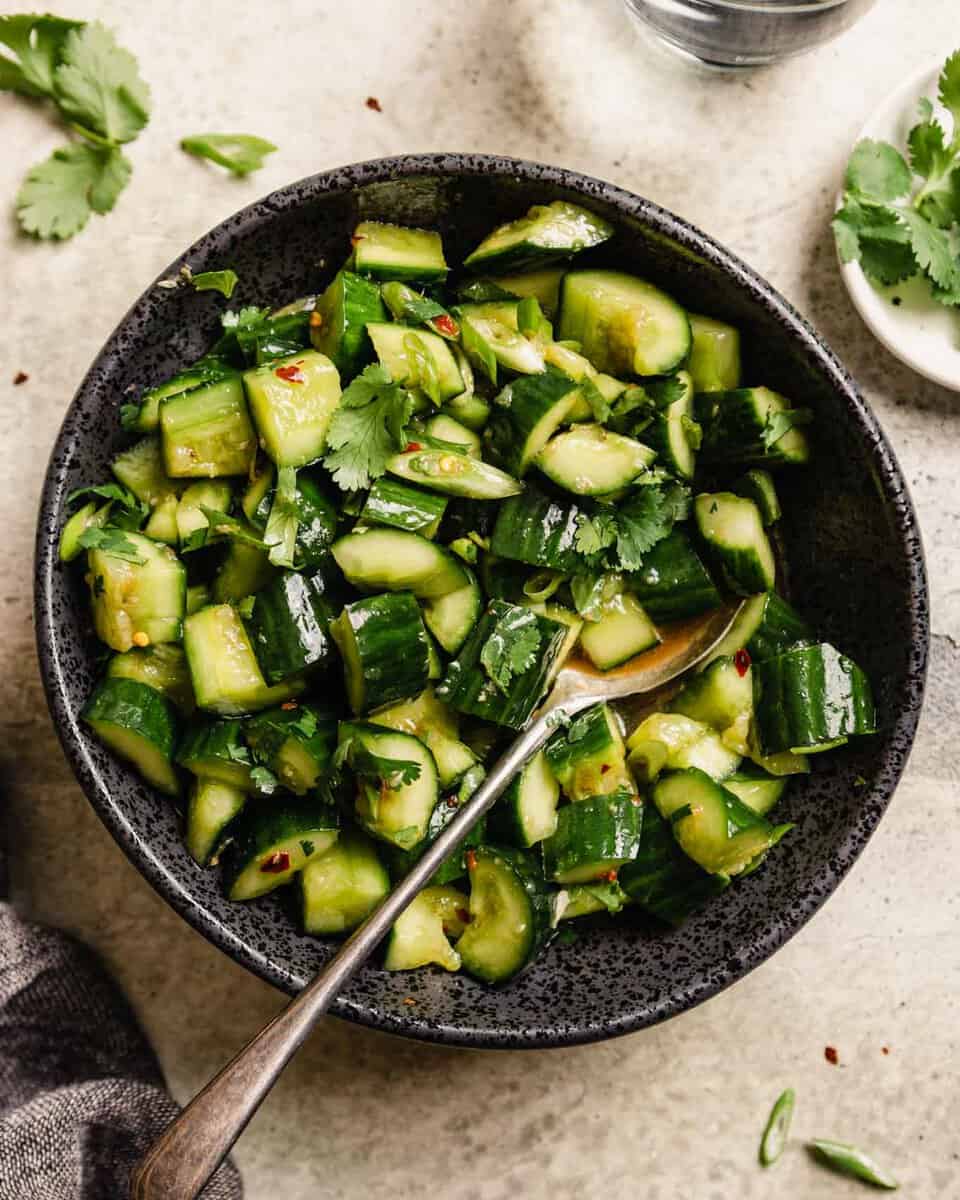 diced cucumbers in a black bowl with a spoon in it—set on a table with cilantro