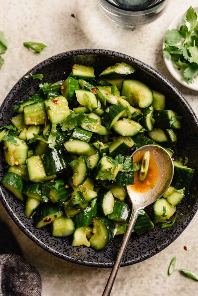 diced cucumbers in a black bowl with a spoon set in the salad filled with dressing 