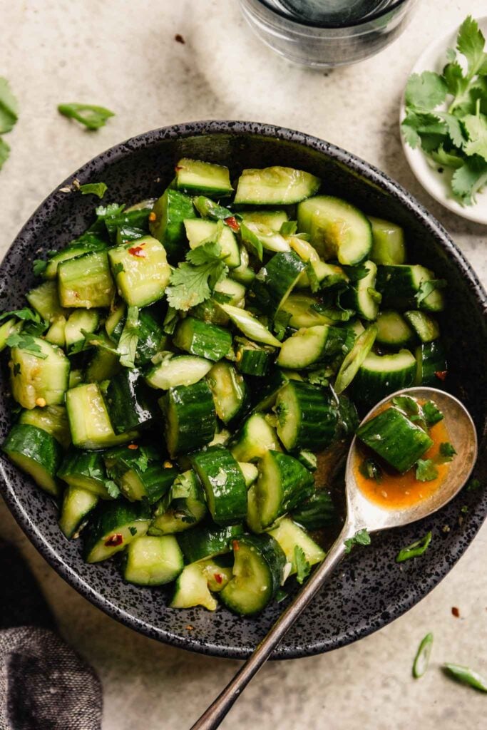 diced cucumbers in a black bowl with a spoon set in the salad filled with dressing