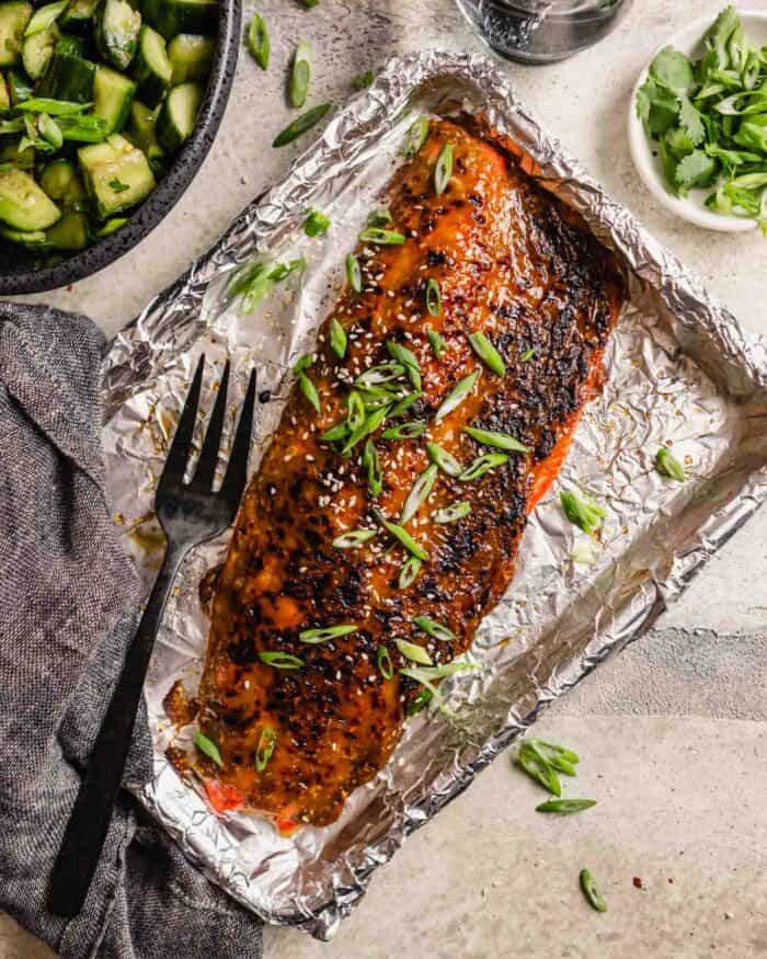 roasted glazed salmon fillet on a foil-lined baking sheet with sliced green onions and sesame seeds sprinkled over top