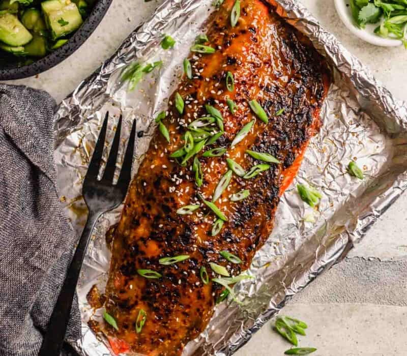 roasted glazed salmon fillet on a foil-lined baking sheet with sliced green onions and sesame seeds sprinkled over top