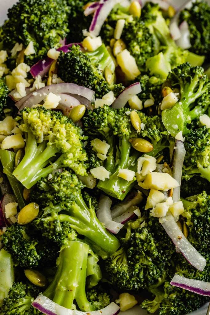 close up of broccoli salad tossed with red onions, cheddar and pepitas 