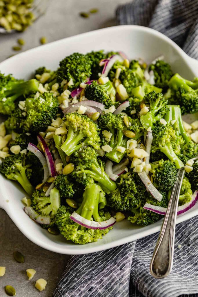 broccoli salad with pepitas, red onion and crumbled cheese in a square white bowl