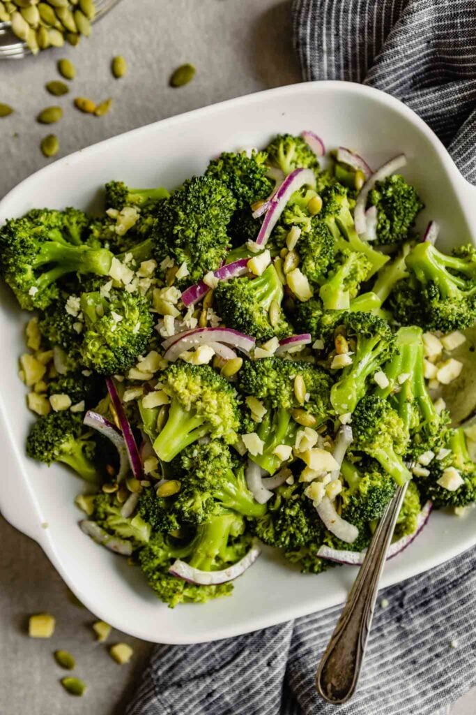 broccoli salad with pepitas, red onion and crumbled cheese in a square white bowl 