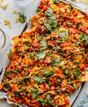 shredded chicken nachos on a sheet pan set on a blue table with colored glasses