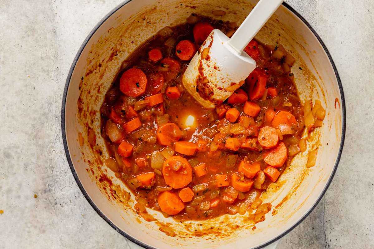 sliced carrots added to a large pot with onions and tomato paste cooking