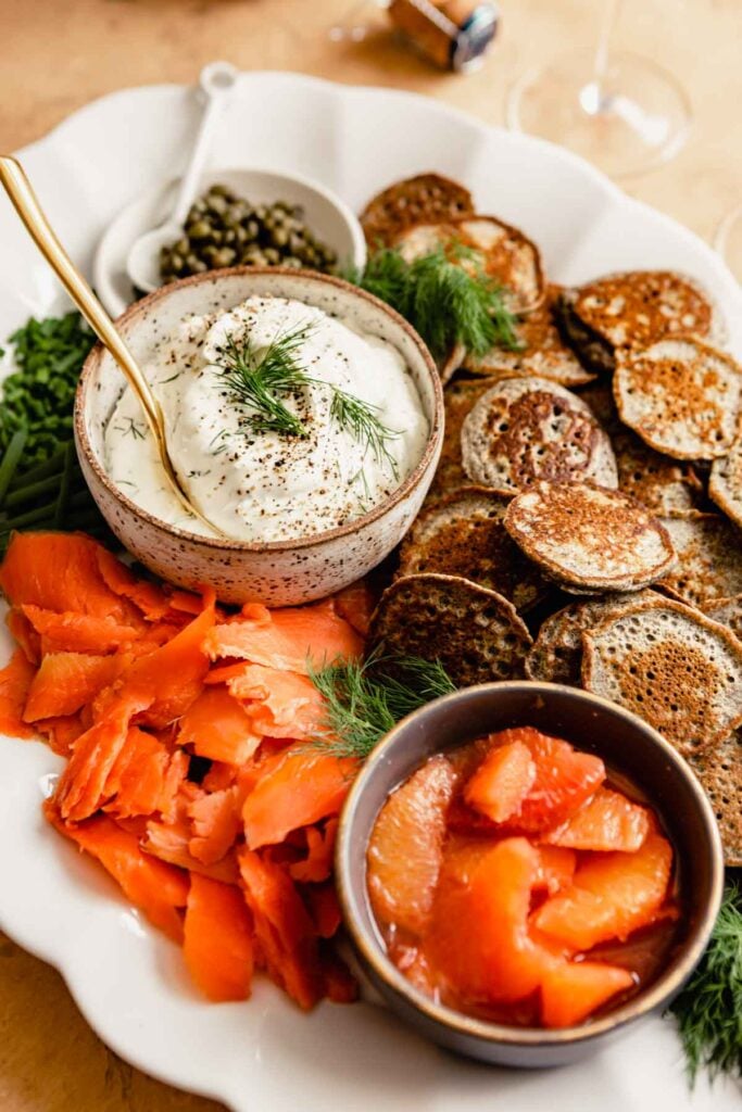small buckwheat pancakes topped with cream cheese, salmon, capers and dill on a brown plate