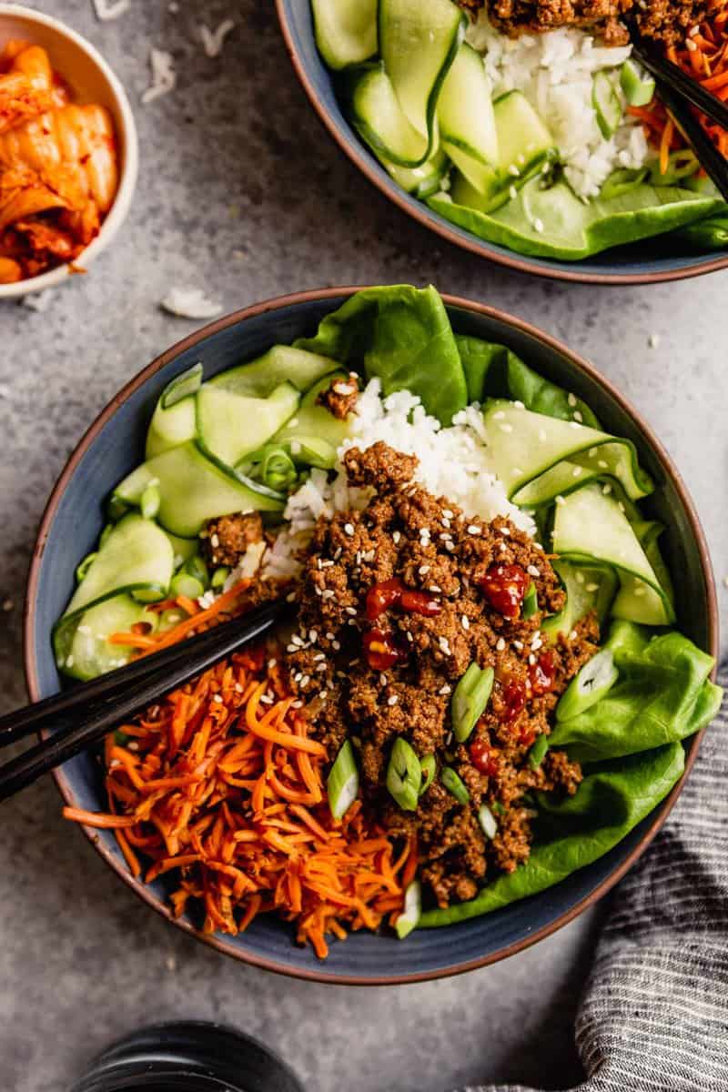 blue bowls filled with ground beef over rice, carrots and cucumbers