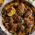 crusted chicken thighs in a skillet with olives, sauce, and lemon wedges