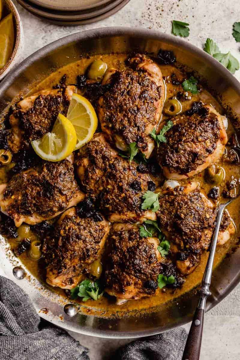 crusted chicken thighs in a skillet with olives, sauce, and lemon wedges