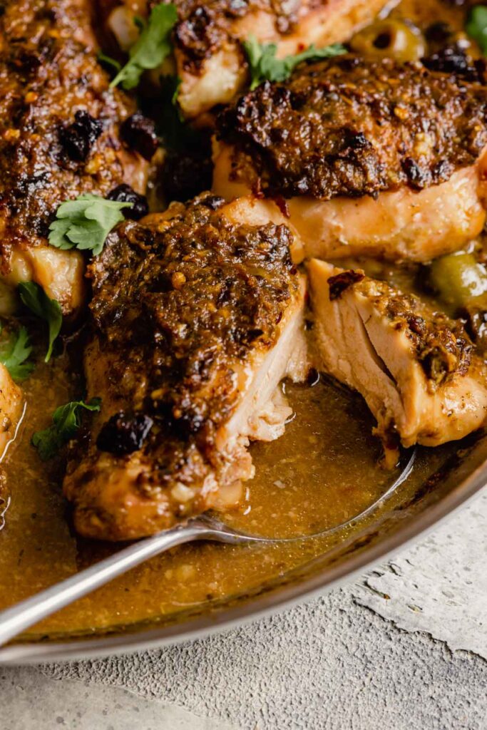 close up image of crusted chicken thighs in a skillet with sauce and olives