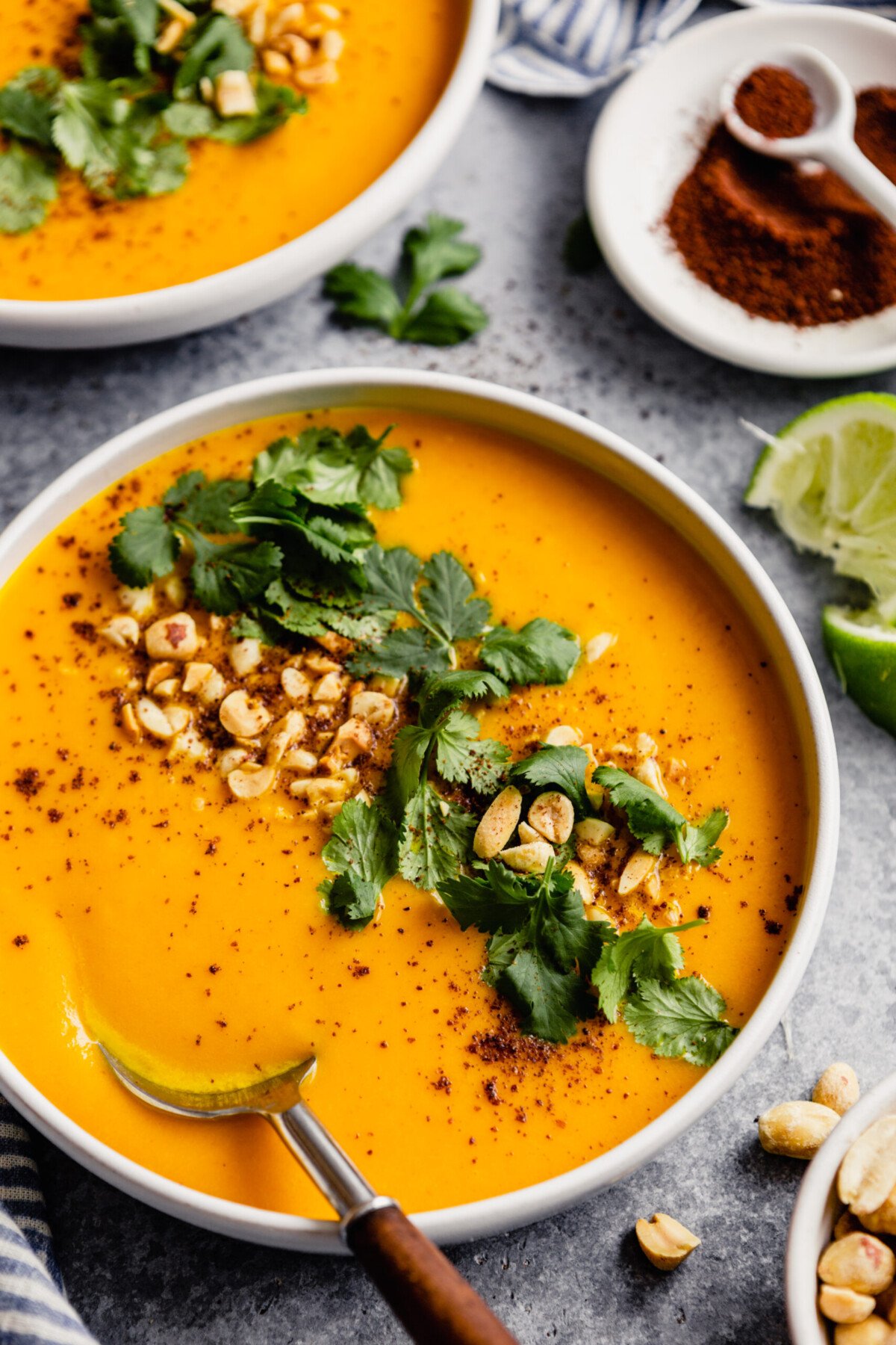 white bowl filled with an orange pureed soup topped with chopped peanut, cilantro and sumac