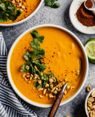 white bowl filled with an orange pureed soup topped with chopped peanut, cilantro and sumac