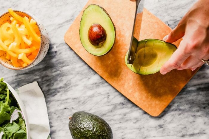 hands cutting an avocado on a small brown cutting board