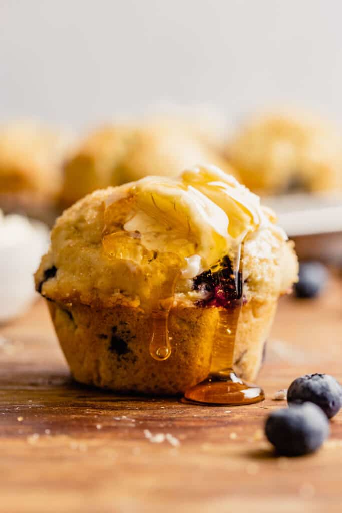a blueberry muffin set on a brown table with honey dripping down it.
