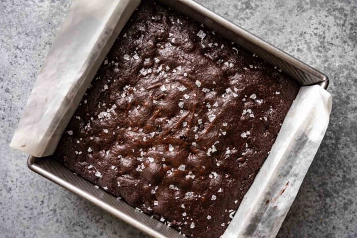 brownies in a baking pan with flaky sea salt sprinkled over top