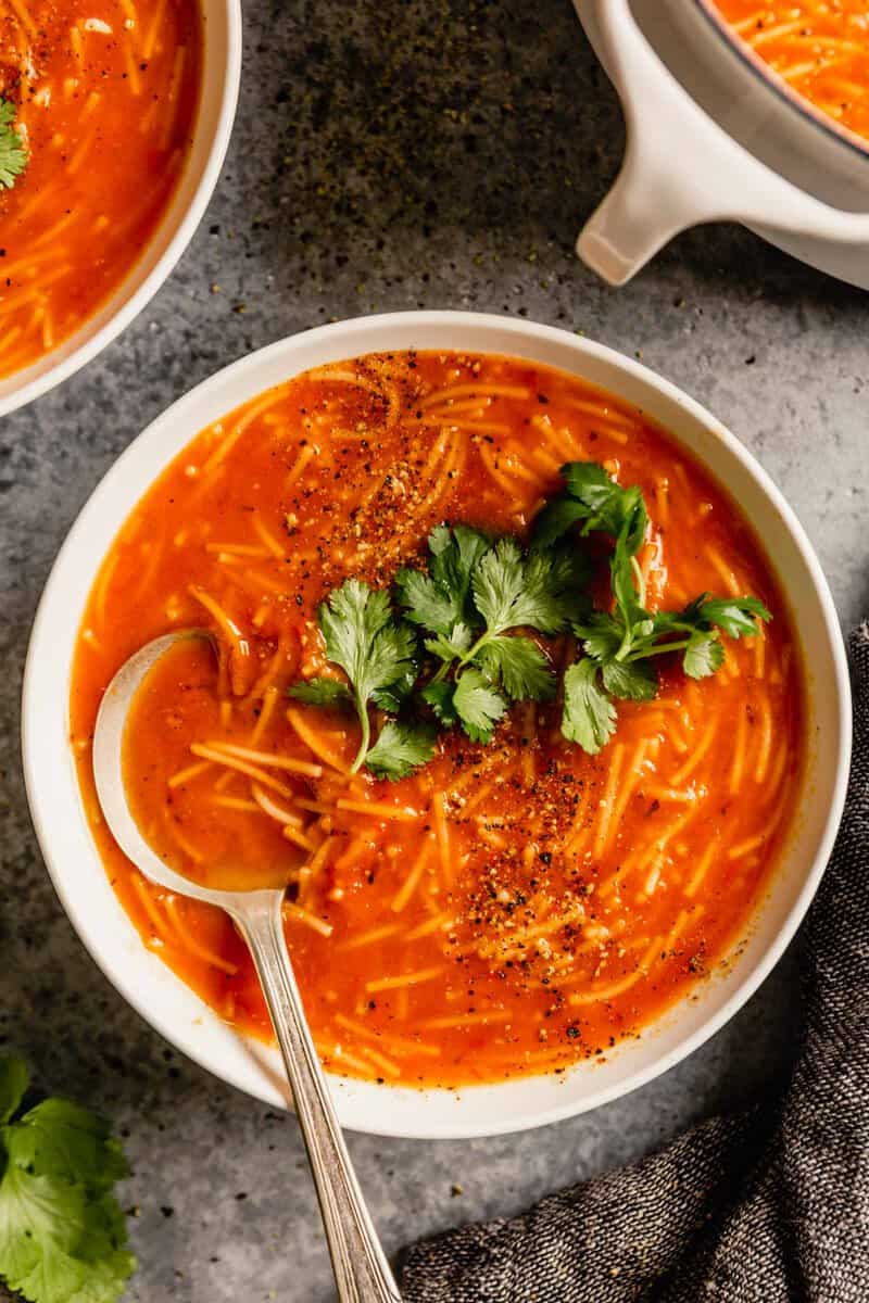 overhead image of a white bowl filled with a tomato noodle soup and topped with cilantro