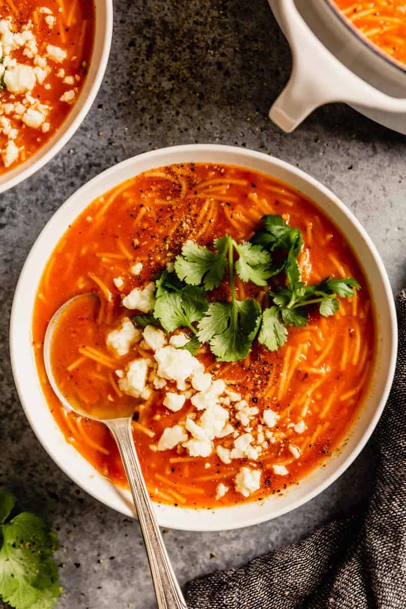 white bowl filled with tomato and noodle soup and topped with cilantro and crumbled cheese