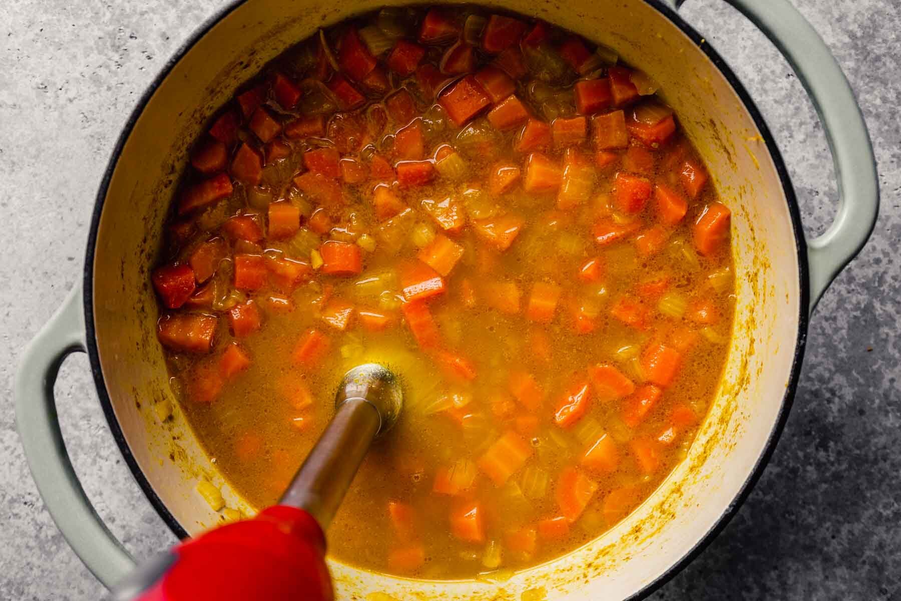immersion blender blending curried carrot soup in a large dutch oven