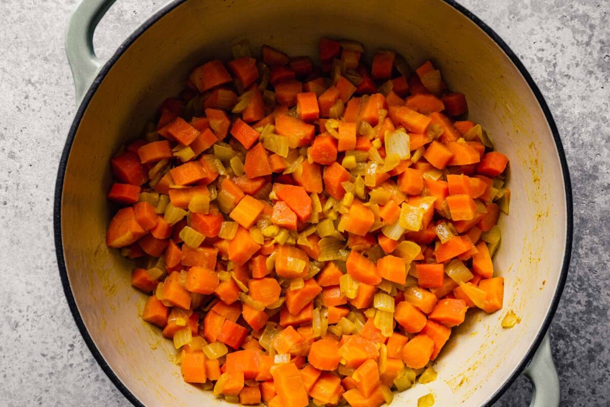 cooked carrots, onions and ginger coated in curry powder in a pot