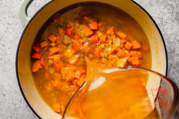 broth being poured over cooked carrots, onions and ginger