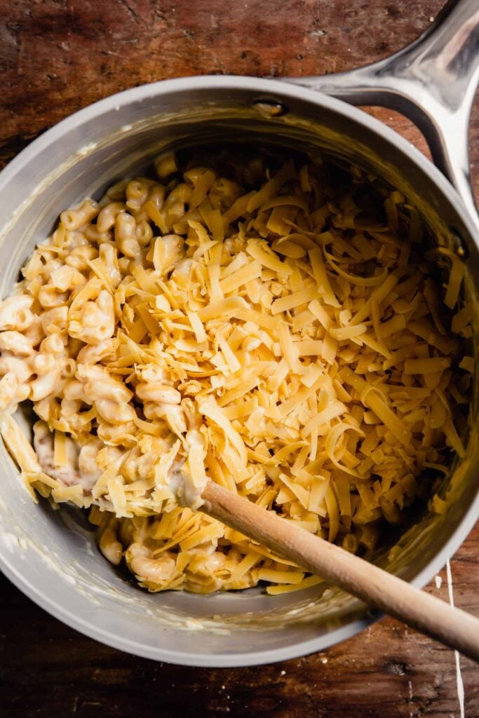 saucy noodles in a saucepan topped with shredded cheese