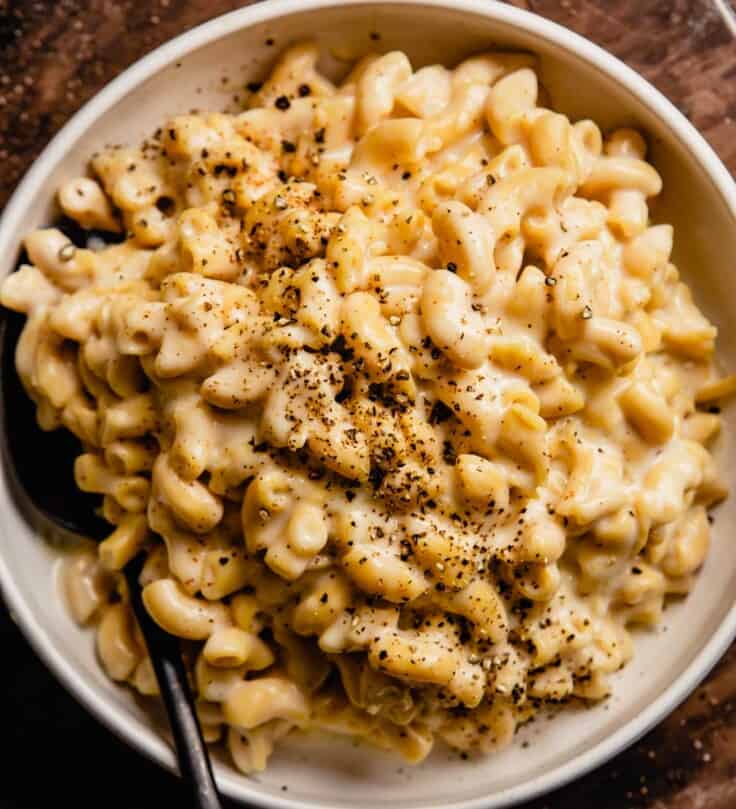 cheesy pasta in a white bowl topped with cracked pepper