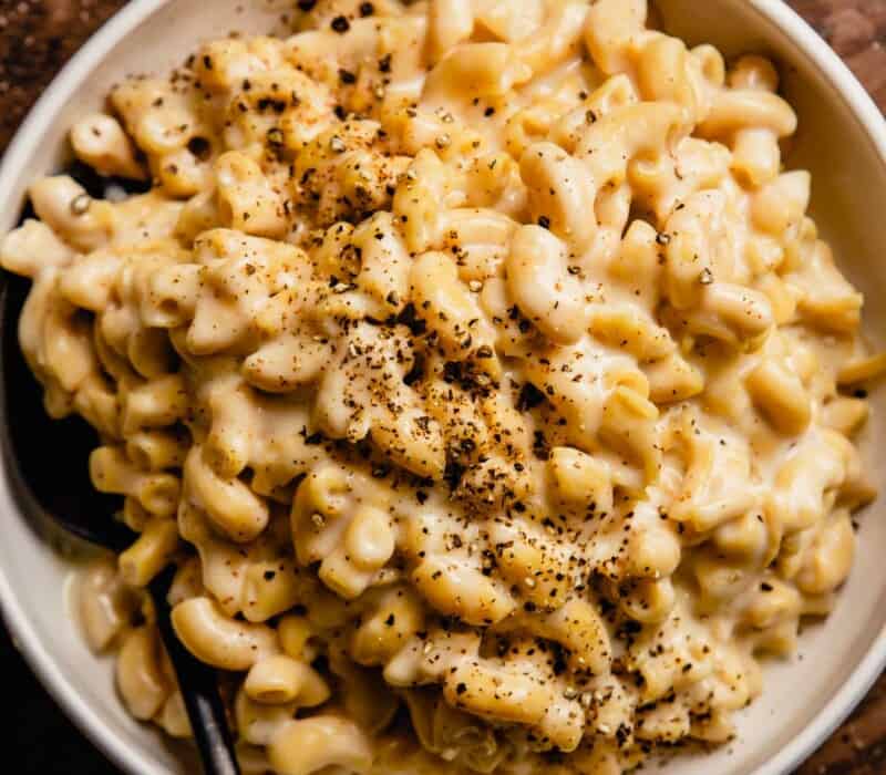 cheesy pasta in a white bowl topped with cracked pepper