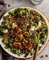 kale and lentil salad in a white bowl set on a wood board topped with feta cheese and toasted almonds