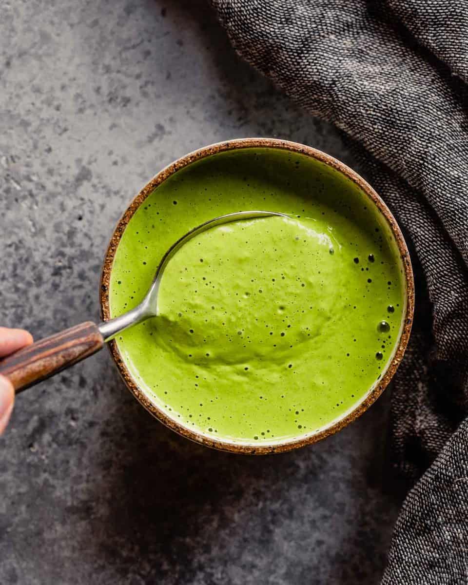 bright green dressing in a white and brown bowl with a spoon being dipped in it