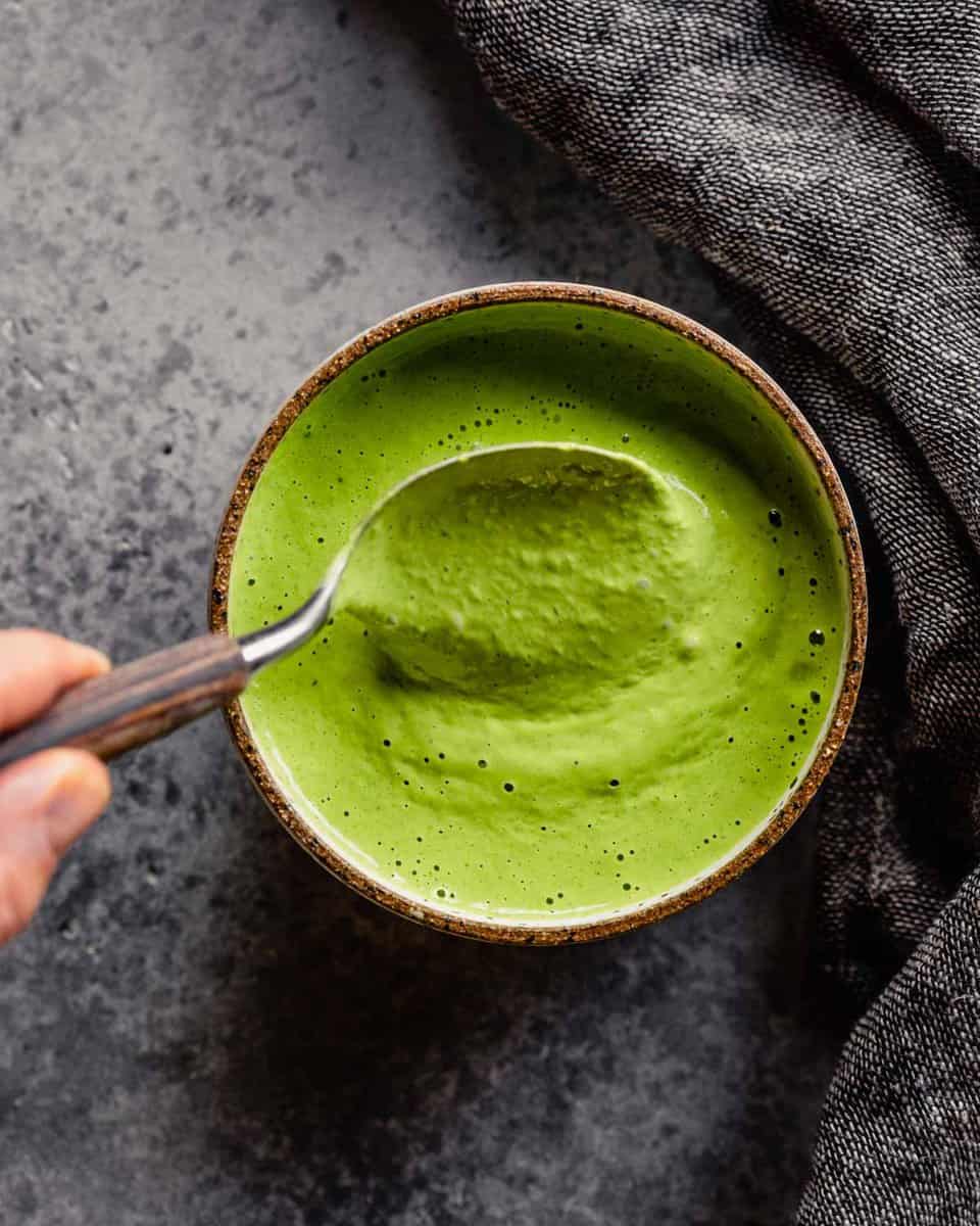 bright green dressing in a white and brown bowl with a spoon being dipped in it