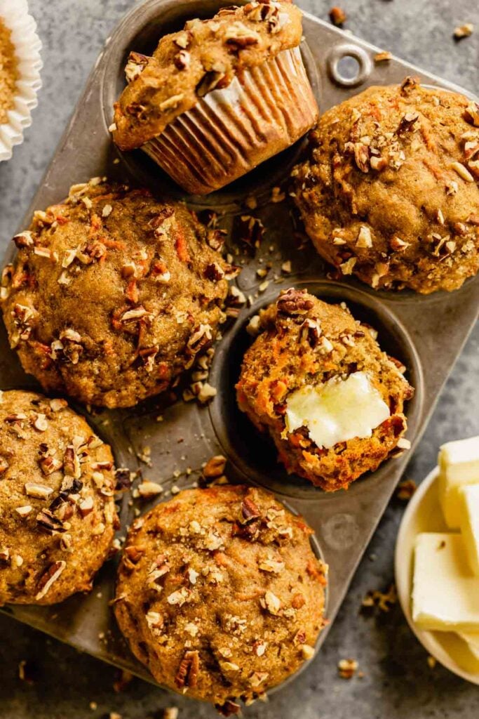 muffins in a muffin tin with pecans scattered around and butter set next to it