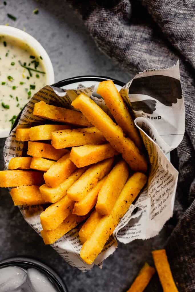 polenta fries piled in a metal bowl with a newspaper 