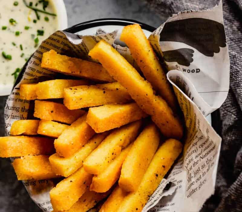 polenta fries piled in a metal bowl with a newspaper