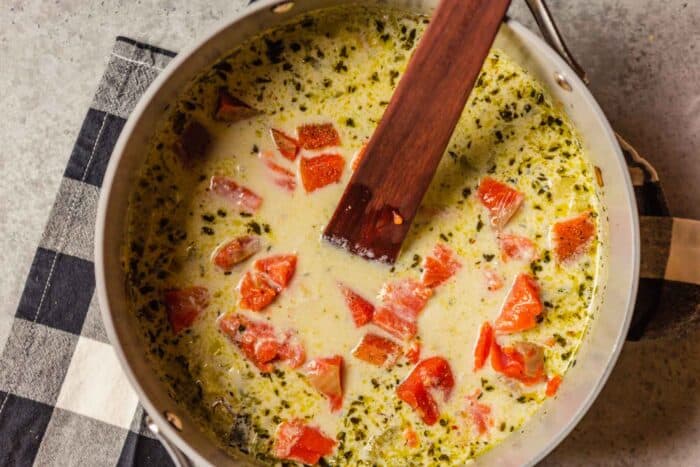 chunks of salmon and vegetables in a creamy broth in a large pot with a wooden spoon