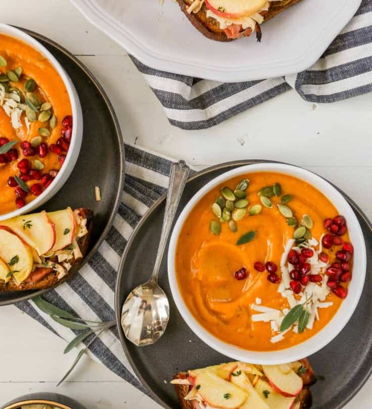 butternut squash soup in shallow white bowls with cheesy apple toasts set around the bowls