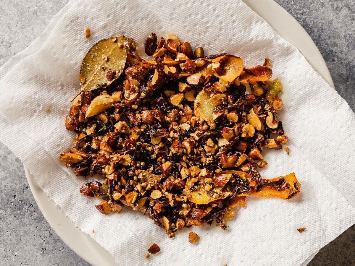 Toasted lemon peel, sliced scallion whites, smashed garlic, chopped almonds and cumin seeds draining on a paper-towel-lined plate. 