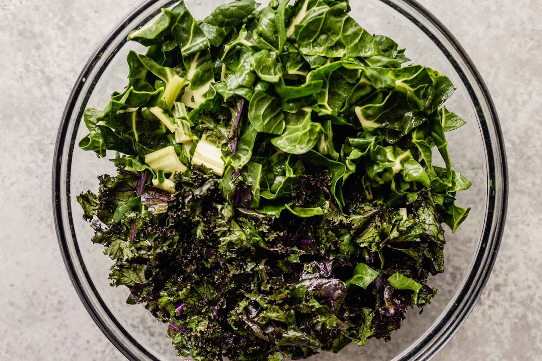 Swiss chard and massaged kale in a large glass mixing bowl.