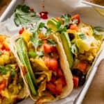 breakfast tacos filled with scrambled eggs, black beans, tomatoes, avocado slices and cilantro set on parchment paper-lined trays
