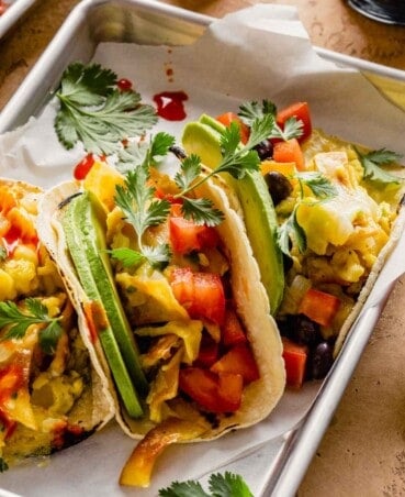 breakfast tacos filled with scrambled eggs, black beans, tomatoes, avocado slices and cilantro set on parchment paper-lined trays