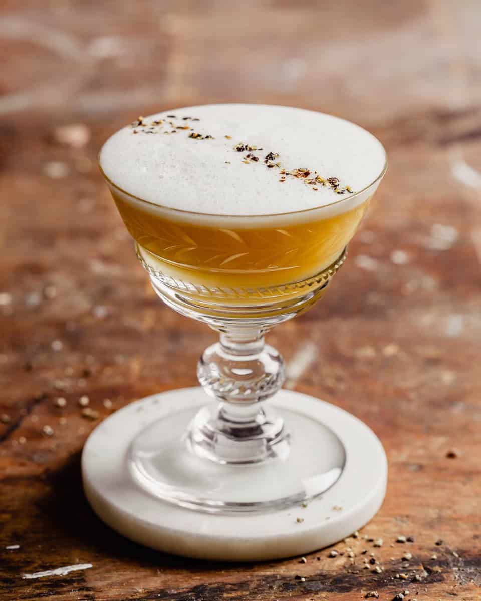 A yellow-colored dink in a coupe-style glass with a foam layer on top