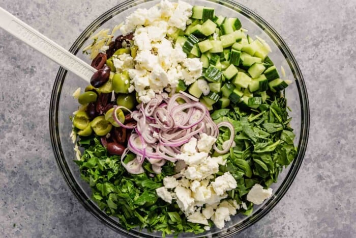 olives, shallots, cucumber, spinach, and feta piled into a large glass bowl
