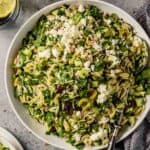 orzo pasta salad with spinach, olives and cucumbers in a large white bowl