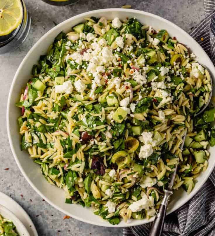 orzo pasta salad with spinach, olives and cucumbers in a large white bowl