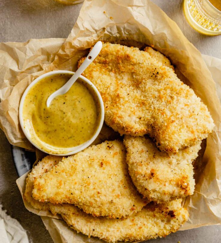 golden brown breaded chicken cutlets in a tray lined with parchment and glasses of beer set around