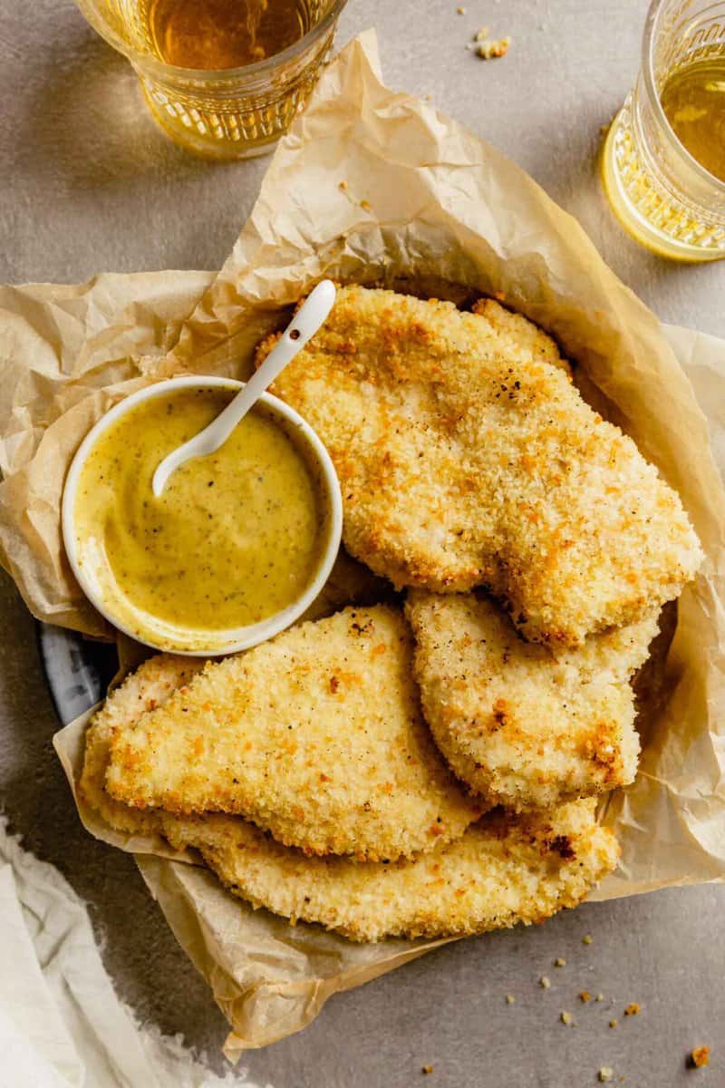 golden brown breaded chicken cutlets in a tray lined with parchment and glasses of beer set around